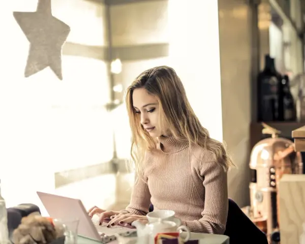Kvinna skriver tack mail efter intervju på sin laptop vid ett bord med en tekanna.