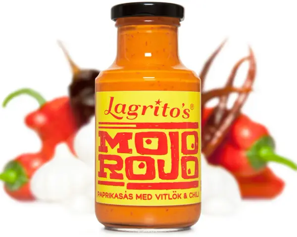 En flaska Lagrito's Mojo Rojo, en paprikasås med vitlök och chili, omgiven av färska chilis och vitlök.