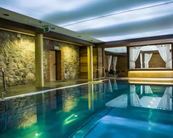 Basen w spa na Kaszubach. Kamienne ściany, turkusowa woda i zaciszne altany z białymi zasłonami tworzą atmosferę relaksu.