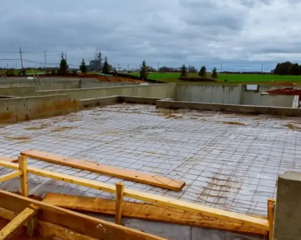 Fundament budowlany z zbrojeniem, przygotowany pod wylanie betonu. Widać betonowe ściany fundamentowe i siatkę stalową na podłożu.