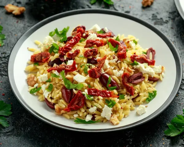 Pyszna sałatka z makaronem orzo, z suszonymi pomidorami, oliwkami, fetą i natką pietruszki. Idealna na lekki posiłek.