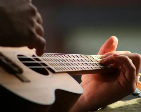 Dłonie grające na ukulele, zbliżenie na gryf i struny.
