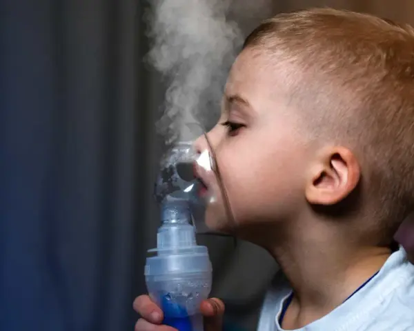 Chłopiec z maską inhalatora na twarzy, wdychający parę.