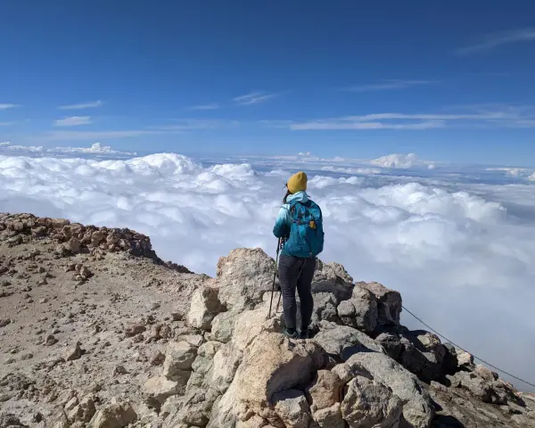 Widok z Teide: turystka w żółtej czapce podziwia morze chmur z wulkanicznego szczytu.