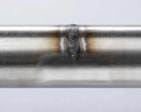 Dettaglio di una saldatura acciaio inox su un tubo metallico, con sfumature iridescenti intorno al cordone.