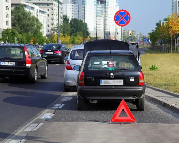 Czarny Opel z otwartą klapą bagażnika i trójkątem ostrzegawczym na autostradzie.
