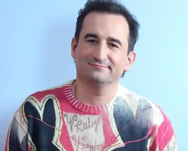 Uśmiechnięty polski aktor z autyzmem w kolorowym swetrze z sercem i napisem "Yo Baby".