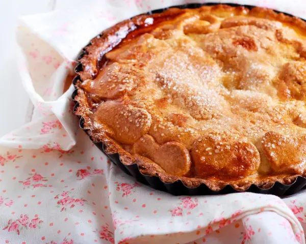 Une délicieuse tarte au sucre dorée, saupoudrée de cristaux de sucre, repose sur une serviette à motifs floraux roses.