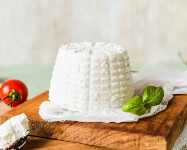Świeża ricotta na desce, obok pomidorki i bazylia. Niskie ricotta kalorie czynią ją idealną dla dbających o linię.
