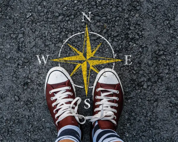 Feet stand on a compass, symbolizing the start of a journey. This image can represent the **mission creep meaning**, where initial goals expand unexpectedly.
