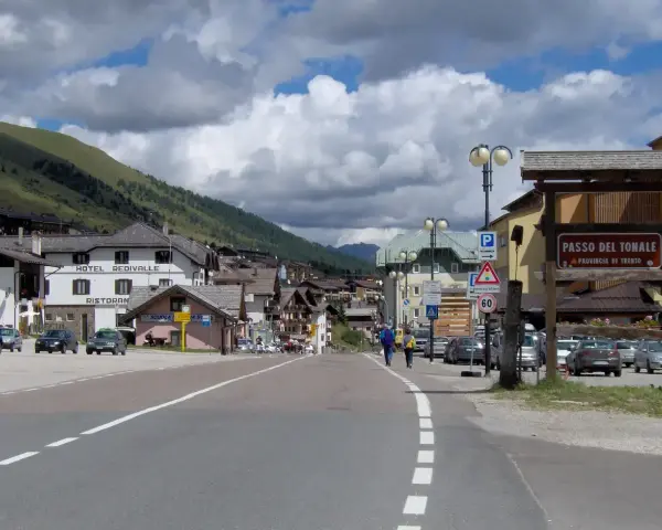 Strada verso il Passo del Tonale in moto, con case alpine e montagne sullo sfondo.