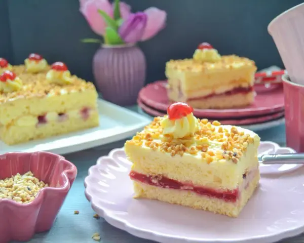 Stückchen eines Frankfurter Kranz Blechs mit Buttercreme, Kirschen und gehackten Nüssen.