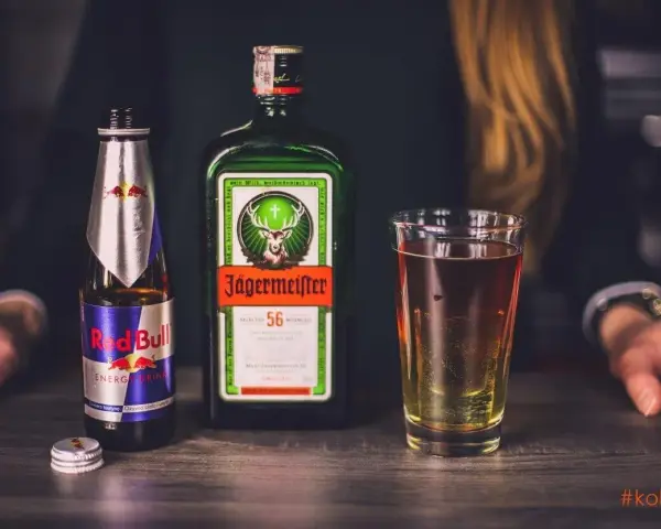 Butelka Jägermeister, puszka Red Bull i szklanka z drinkiem. Jägermeister to niemiecki likier ziołowy, często mieszany z napojami energetycznymi.