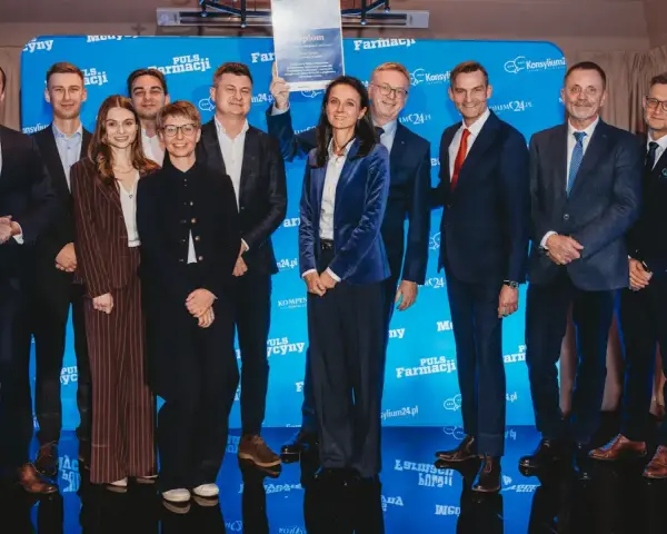 Grupa ludzi na scenie, wśród nich Janusz Sowa, odbiera dyplom. W tle niebieskie banery z logo Puls Farmacji.