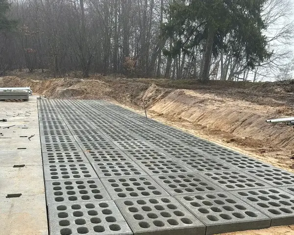 Trwa utwardzenie terenu. Betonowe płyty z otworami tworzą nawierzchnię obok placu budowy z materiałami.