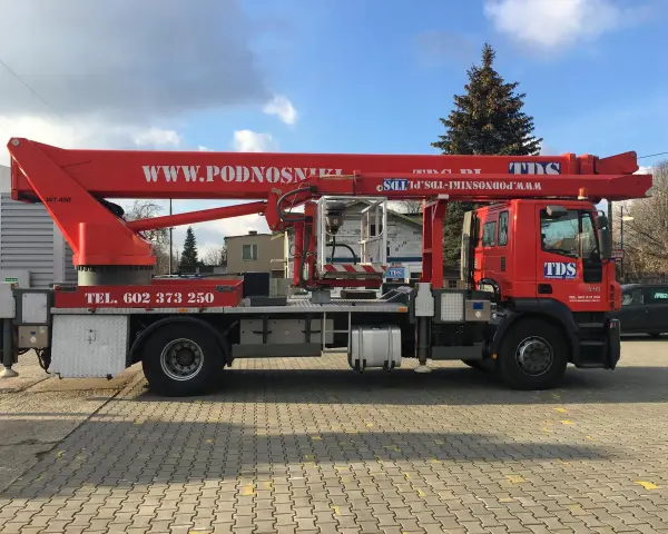 Czerwony podnośnik koszowy WUMAG WT 450 z koszem roboczym i wysięgnikiem. Na pojeździe widnieje napis WWW.PODNOSNIKI-TDS.PL.
