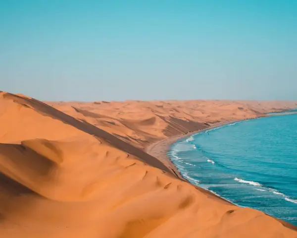 Piaskowe wydmy Namibii spotykają się z turkusowym oceanem. Idealna namibia pogoda na podziwianie tego kontrastu.