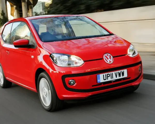 Czerwony Volkswagen up! pędzi po miejskiej drodze, odbijając światła miasta w swojej lśniącej karoserii.