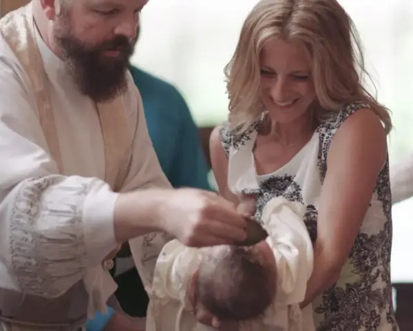 A priest performs a baptism, pouring water on a baby's head. The mother smiles, holding her child. This image captures the sacred moment of how to baptize someone.