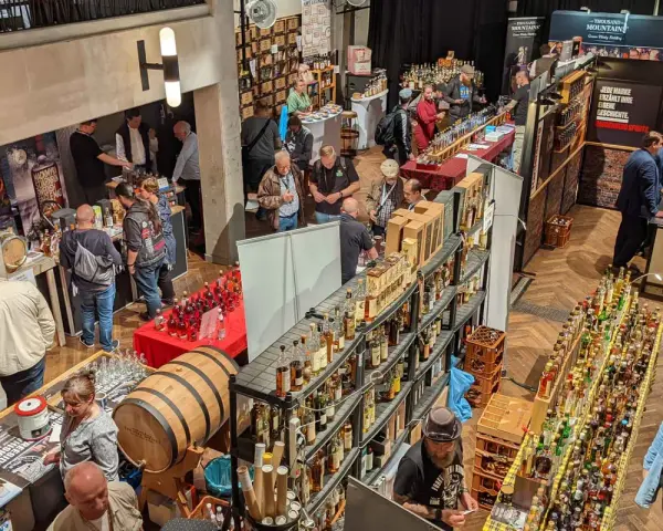 Besucher auf einer Messe probieren Spree-side Whisky. Viele Flaschen und ein Fass sind ausgestellt.