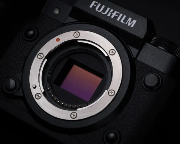 Zbliżenie na matrycę aparatu Fujifilm xh2s, lśniący metalowy pierścień mocowania obiektywu i czerwona kropka sygnalizująca montaż.