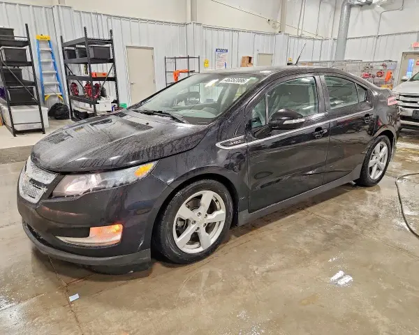 Czarny Chevrolet Volt stoi w garażu, mokry od deszczu. W tle regały z narzędziami i drabina.
