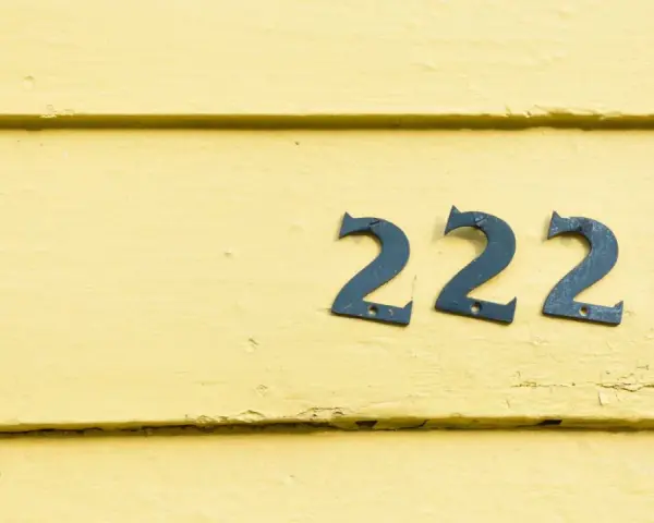 Na żółtej, drewnianej ścianie widnieje anielska liczba 222.