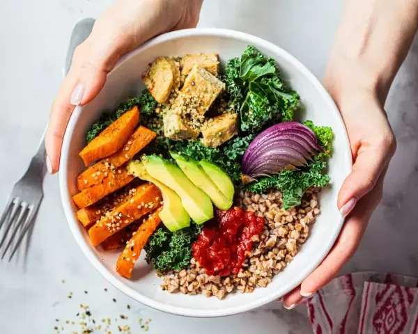 Pyszny bowl z kaszą, pieczonym batatem, awokado, tofu i czerwoną cebulą, polany pikantnym sosem do bowla.