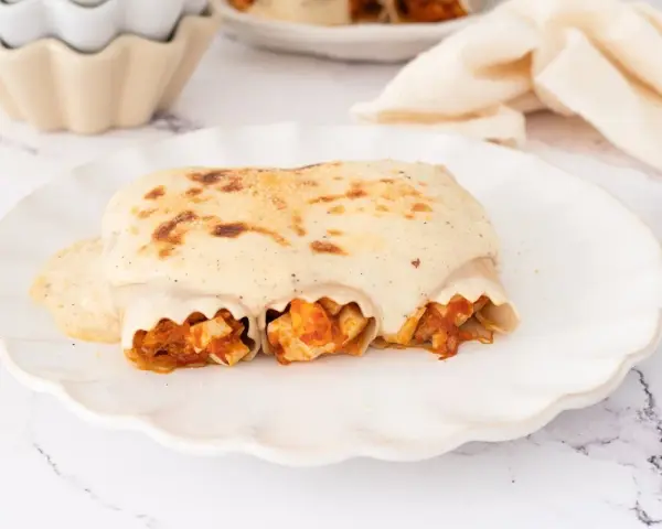 Canelones de atún gratinados con bechamel cremosa, listos para disfrutar en un plato blanco con borde ondulado.