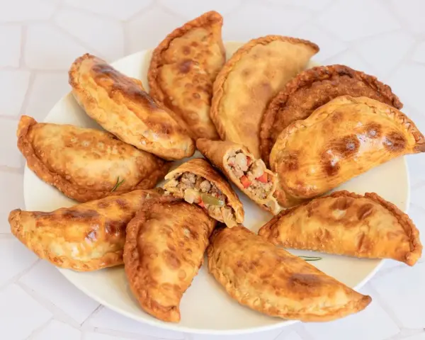 Empanadas de carne doradas y crujientes en un plato, una partida muestra el relleno.