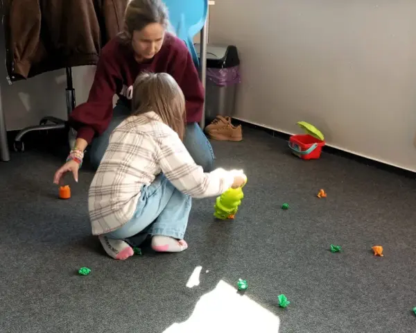 Dzieci bawią się na dywanie, zbierając małe, kolorowe figurki. Www.