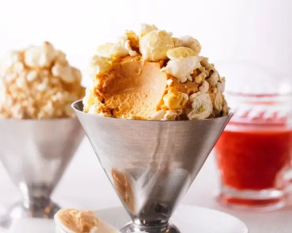 Cremiges Karamell-Popcorn-Eis in einem Metallbecher, garniert mit knusprigem Popcorn. Ein süßer Genuss!