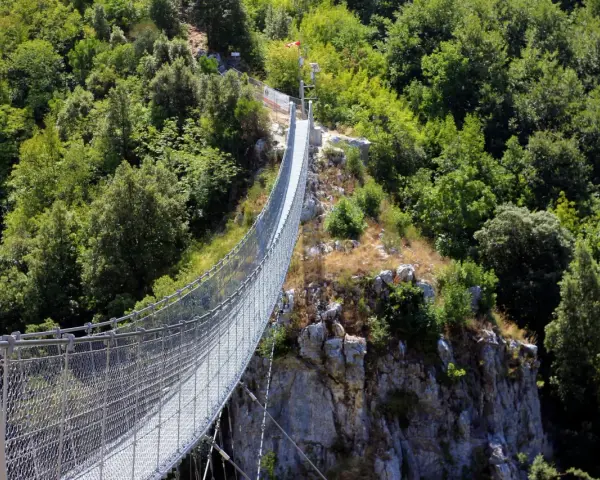 Un avventuroso percorso ponte tibetano si snoda tra rocce e fitta vegetazione, offrendo una vista mozzafiato sulla valle.