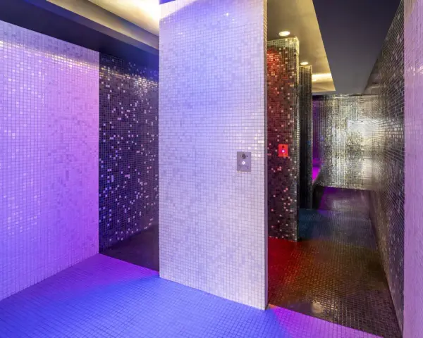 Un espace de détente aux murs recouverts de mosaïques scintillantes, baigné de lumières violettes et bleues. Une invitation à une douche sensorielle immersive.