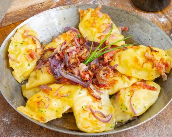 Herzhafte pierogi ruskie, goldgelb und dampfend, garniert mit knusprigem Speck, karamellisierten Zwiebeln und frischem Schnittlauch.