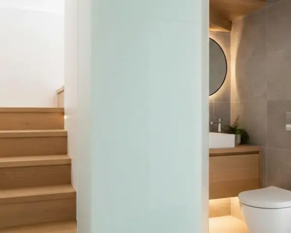 Escaliers en bois menant à un wc sous pente moderne, avec lavabo et miroir rond.