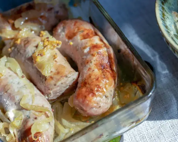 Pyszna biała kiełbasa z piekarnika, pieczona z cebulką i musztardą. Idealna na obiad lub kolację.