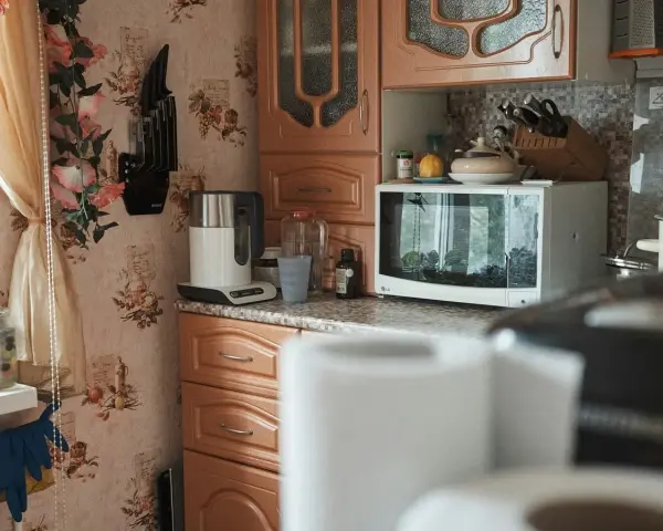 Kuchnia z kwiatową tapetą. Czy mikrofala może stać na lodówce? Tutaj stoi na blacie, obok czajnika i słoików.