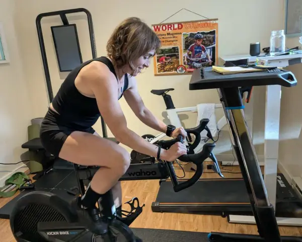 Woman on a Wahoo Kickr bike, a type of spin bike, trains indoors. A treadmill is visible, highlighting the spin bike vs trainer setup.