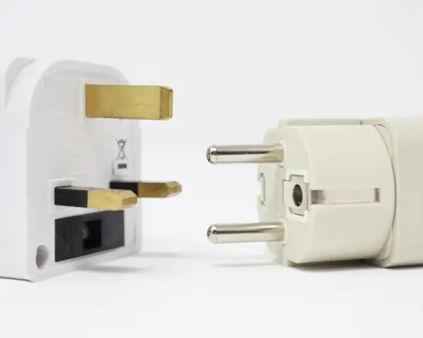 Adaptadores para diferentes tipos de enchufes: uno blanco con tres clavijas doradas y otro beige con dos clavijas plateadas.