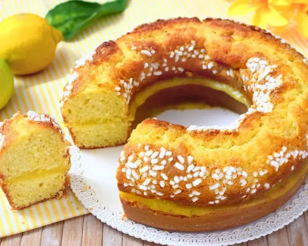 Un soffice ciambellone al limone, con una golosa crema gialla all'interno e decorato con perline di zucchero. Perfetto per la colazione o la merenda.