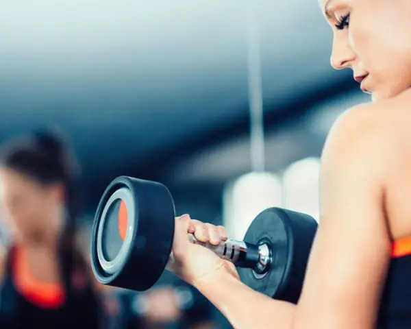 Frau hebt Hantel. Die Frage, wieviel kg darf eine Frau heben arbeitsrecht, ist hier nicht relevant, da es um Fitness geht.
