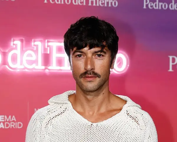 Hombre con un estiloso bigote, perfecto para Movember, luce un jersey blanco de punto.