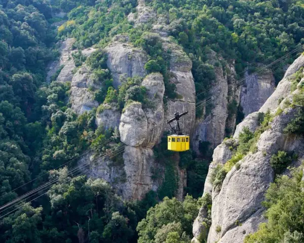 A bright yellow cable car ascends the rugged, tree-covered cliffs of Montserrat, Spain.