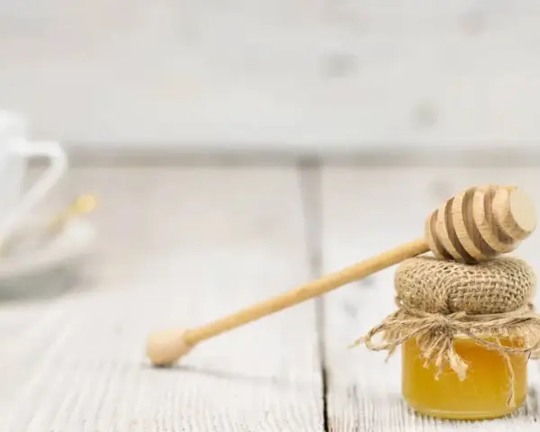 Mały słoiczek miodu z drewnianą chochlą, idealny do herbaty. Warto pamiętać o jego miód kcal.
