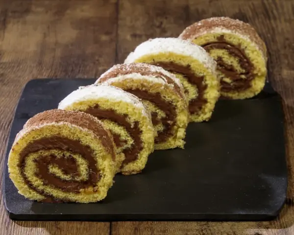 Fette di rotolo alla nutella cosparse di zucchero a velo e cacao, su una lavagna scura, pronte per essere gustate.