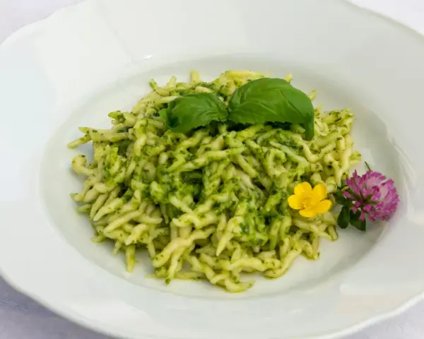 Pasta al pesto con hojas de albahaca fresca y flores comestibles.