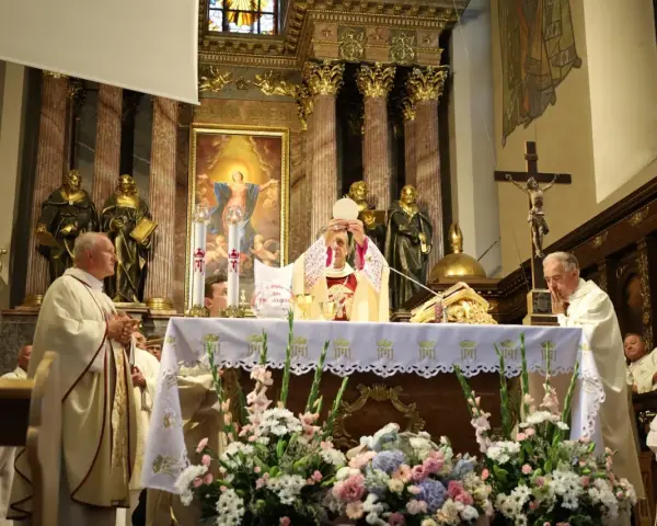 Uroczysta msza święta w kościele. Kapłan podnosi hostię, symbolizując piękna modlitwę do Boga. W tle złote zdobienia i obrazy.