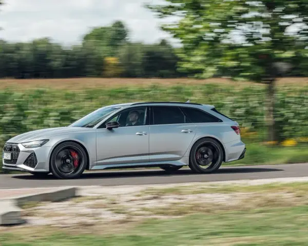 Srebrne Audi RS6 Avant pędzi po wiejskiej drodze, otoczone zielenią pól i drzew.