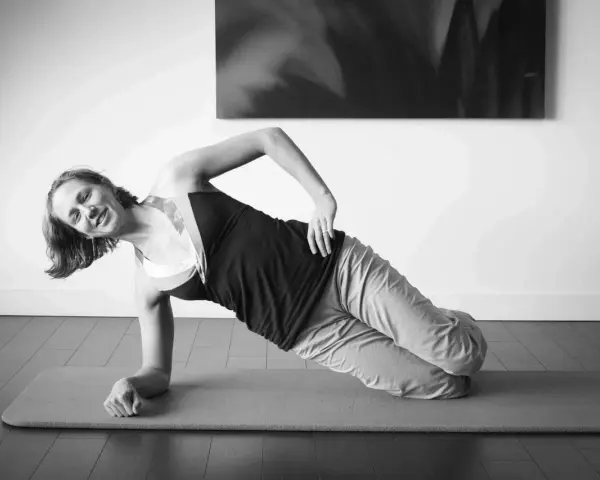 Femme souriante en plein gainage latéral sur un tapis de yoga.